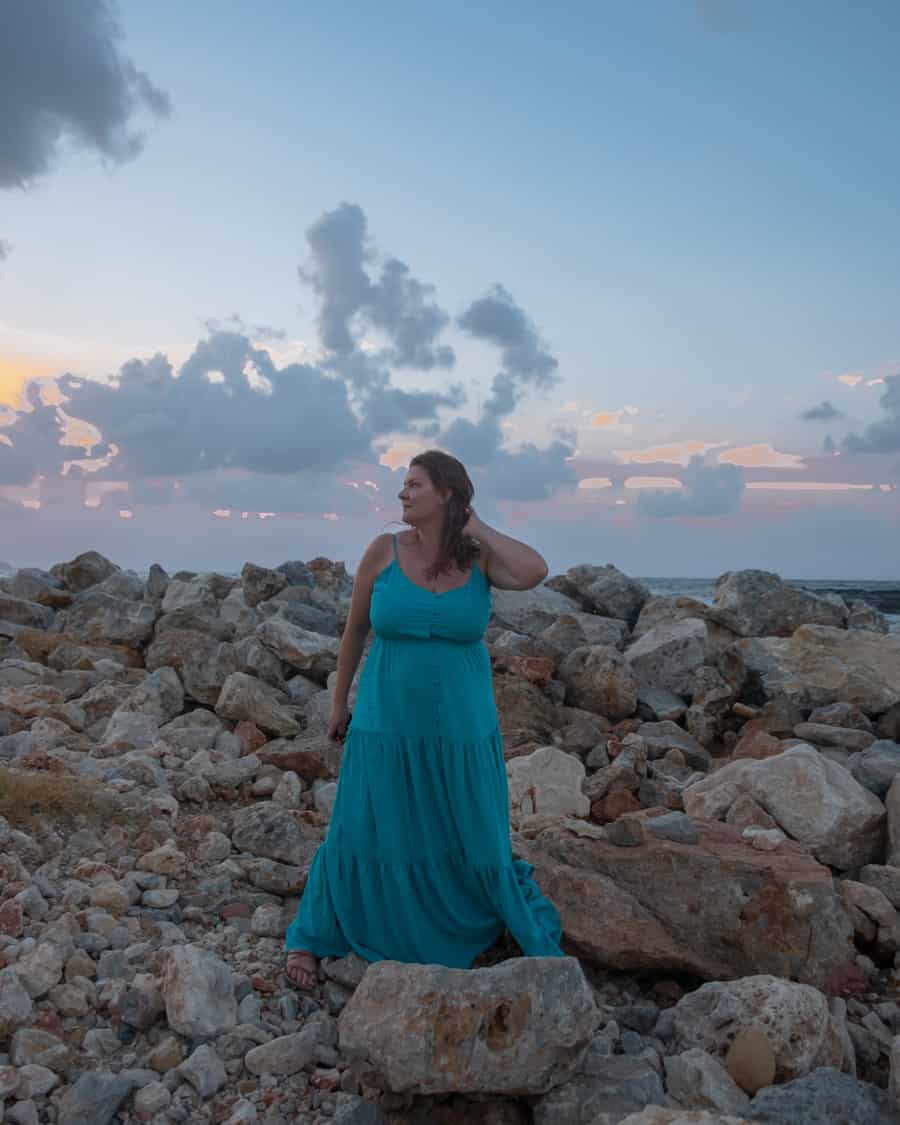 Woman standing solo in Crete on rocks at sunset. 