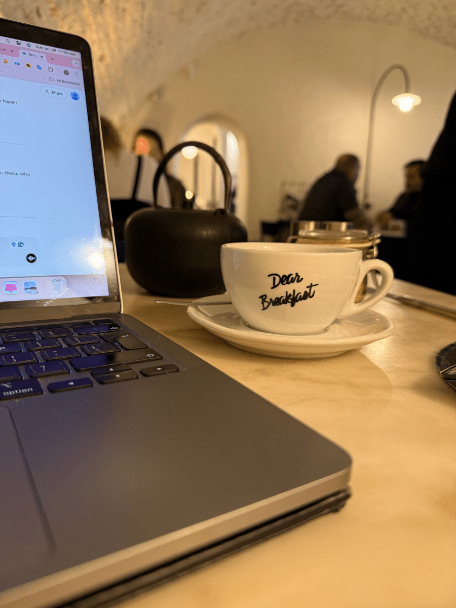 A cozy indoor scene at Dear Breakfast in Paris, showing a laptop next to a cup labeled "Dear Breakfast" on a marble table.