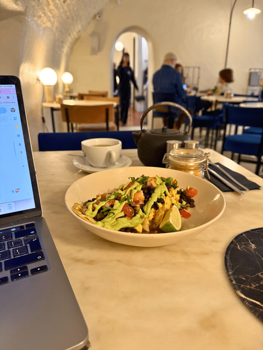 A vibrant breakfast bowl with avocado, beans, and tomatoes on a marble table at Dear Breakfast in Paris, with a laptop and teapot nearby in the cafe's cozy interior.