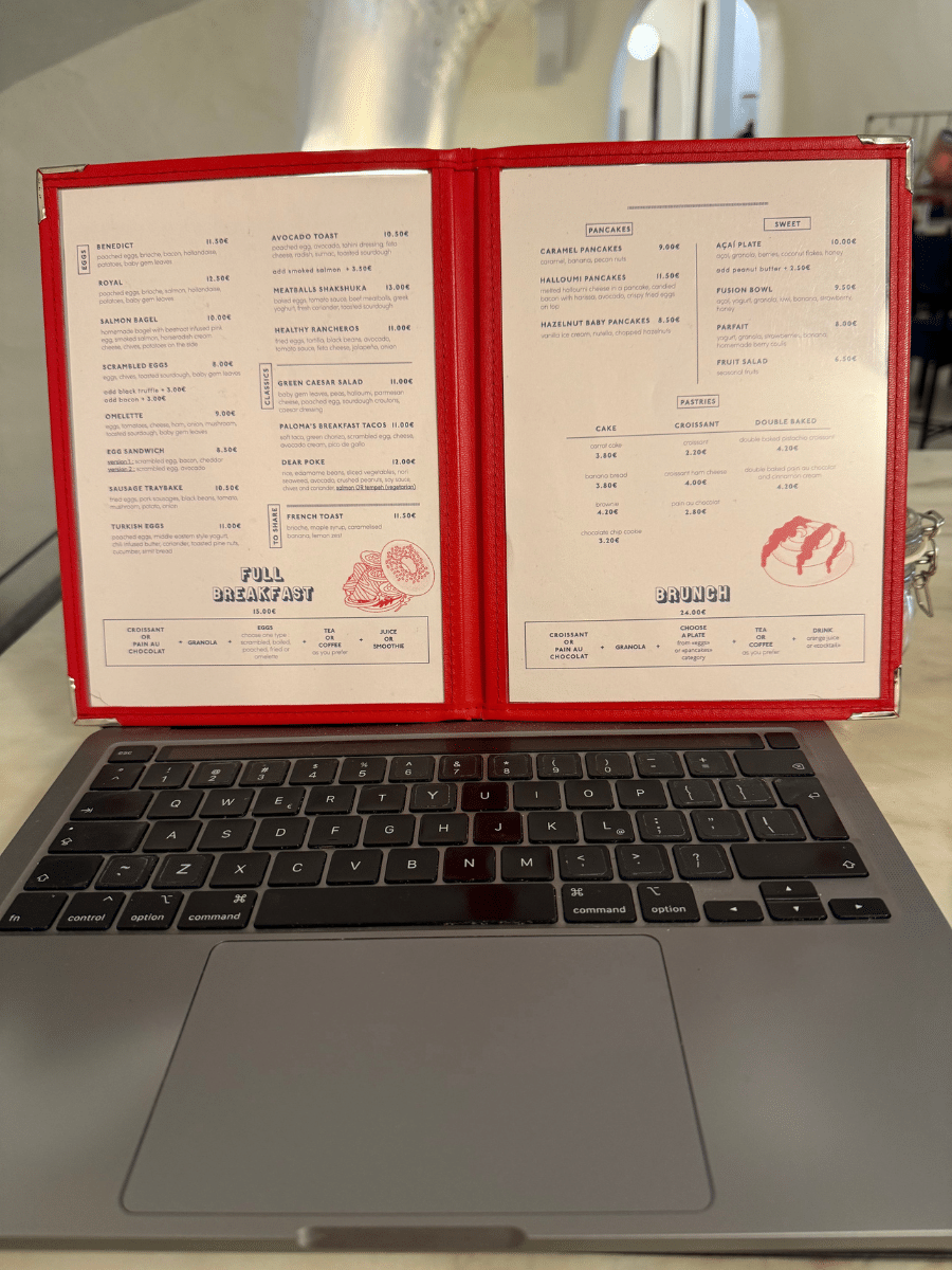 A breakfast menu from "Dear Breakfast Bica," placed on a laptop in a cozy café setting.