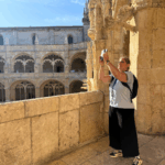 Woman photographing the architectural details from the upper cloister level of Jerónimos Monastery in Lisbon, Portugal