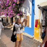 Tourist taking a selfie in front of vibrant purple bougainvillea and colorful Portuguese street wall in Óbidos, Portugal