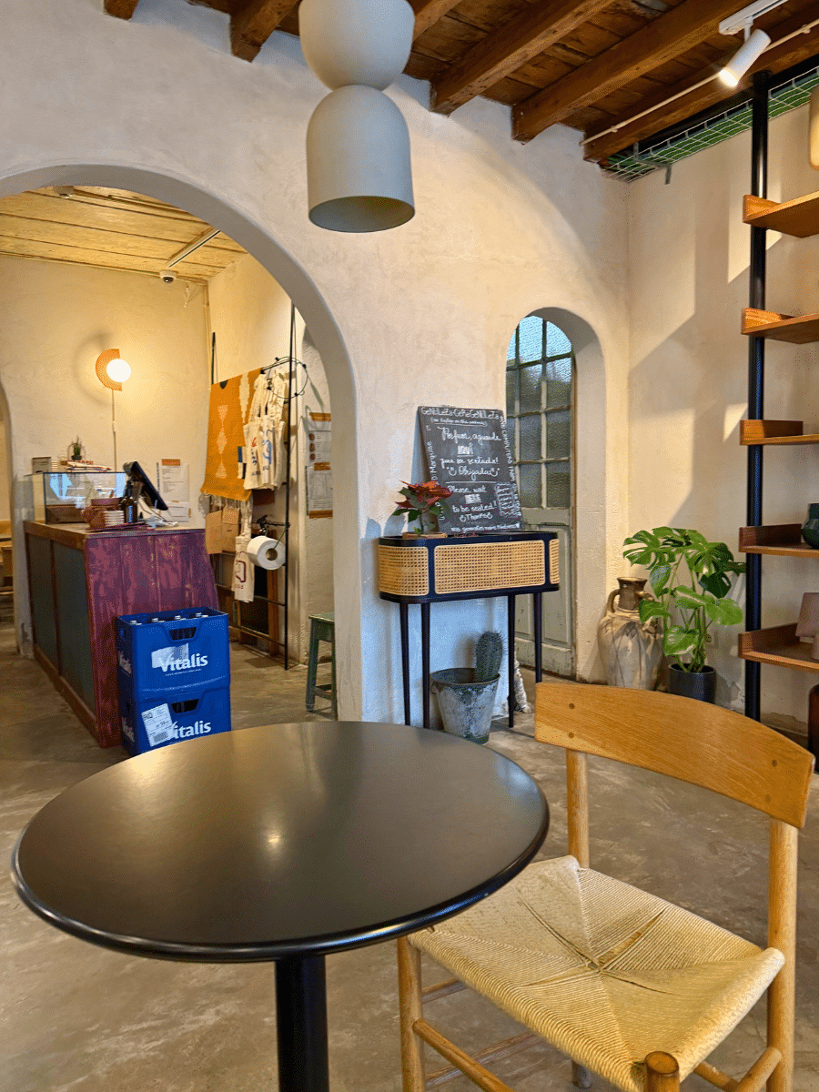 Interior of Marquise cafe, featuring a wooden chair and a round black table in the foreground. The space is decorated with natural tones, arches, and rustic accents, creating a welcoming atmosphere.