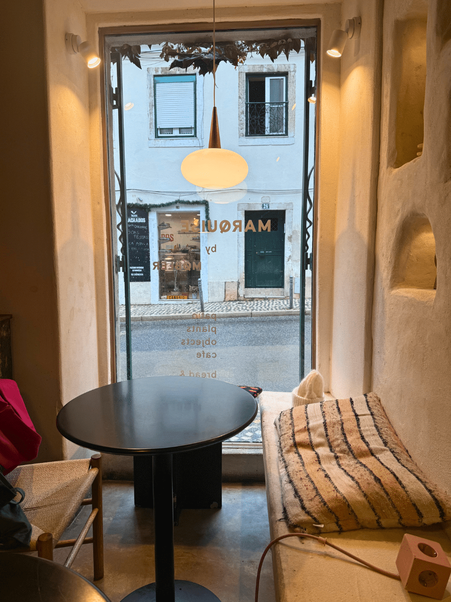 Cozy corner at Marquise cafe, showcasing a minimalist seating area with a black round table, a wooden chair, and a cushioned bench by a large window overlooking the street.
