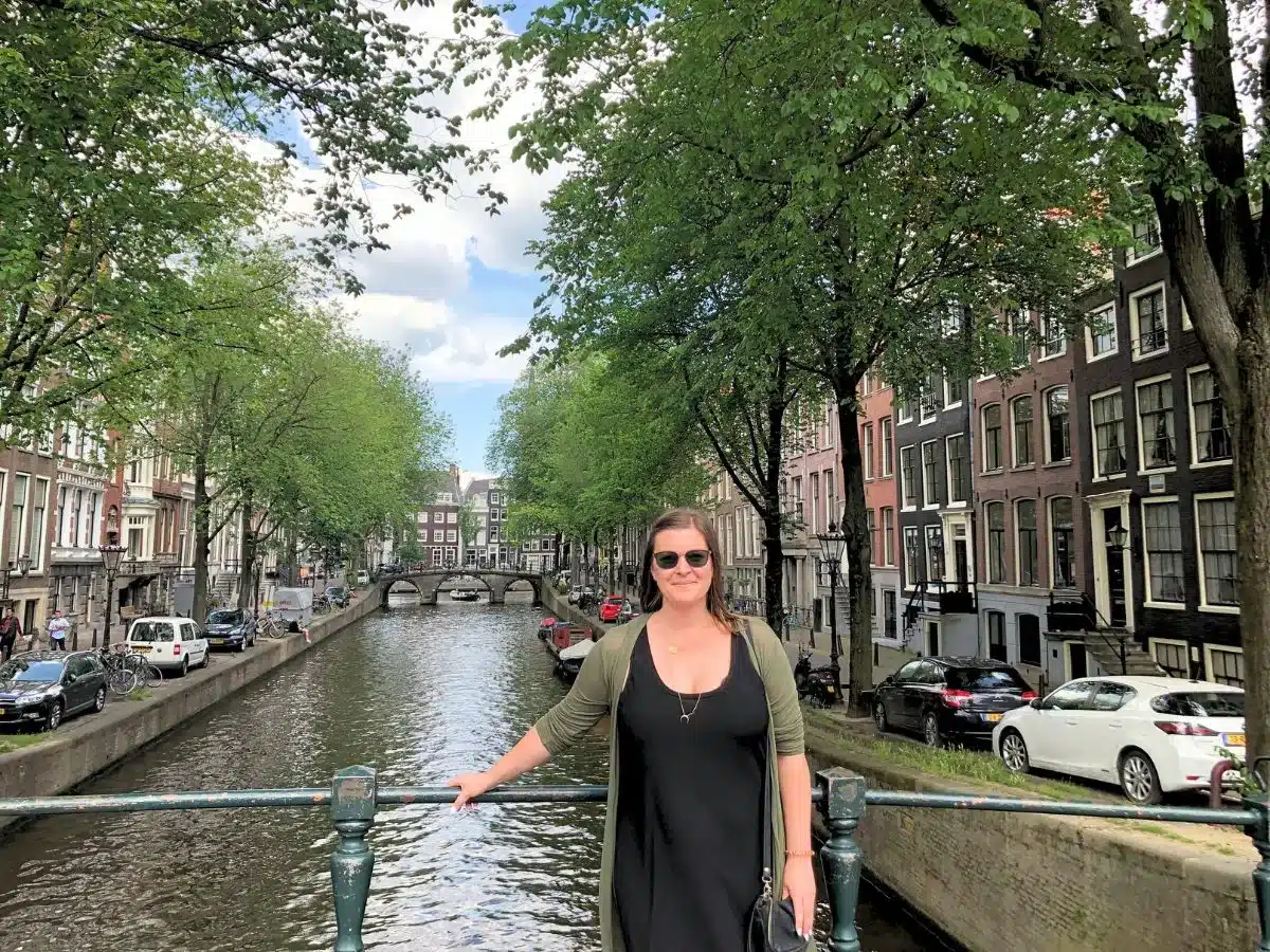 A woman alone in Amsterdam standing at the canal with little boats in background. 