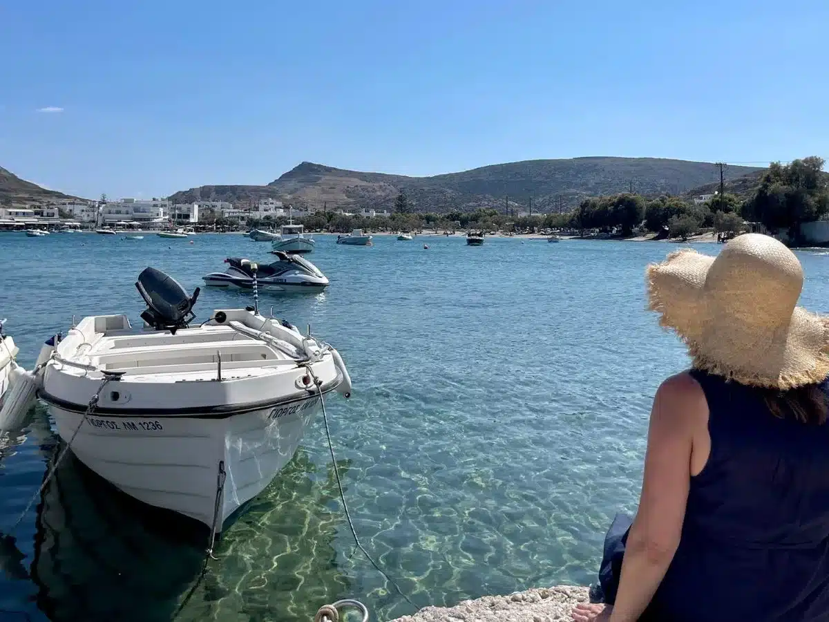 A woman sitting by the sea in Milos with a a boat in the water