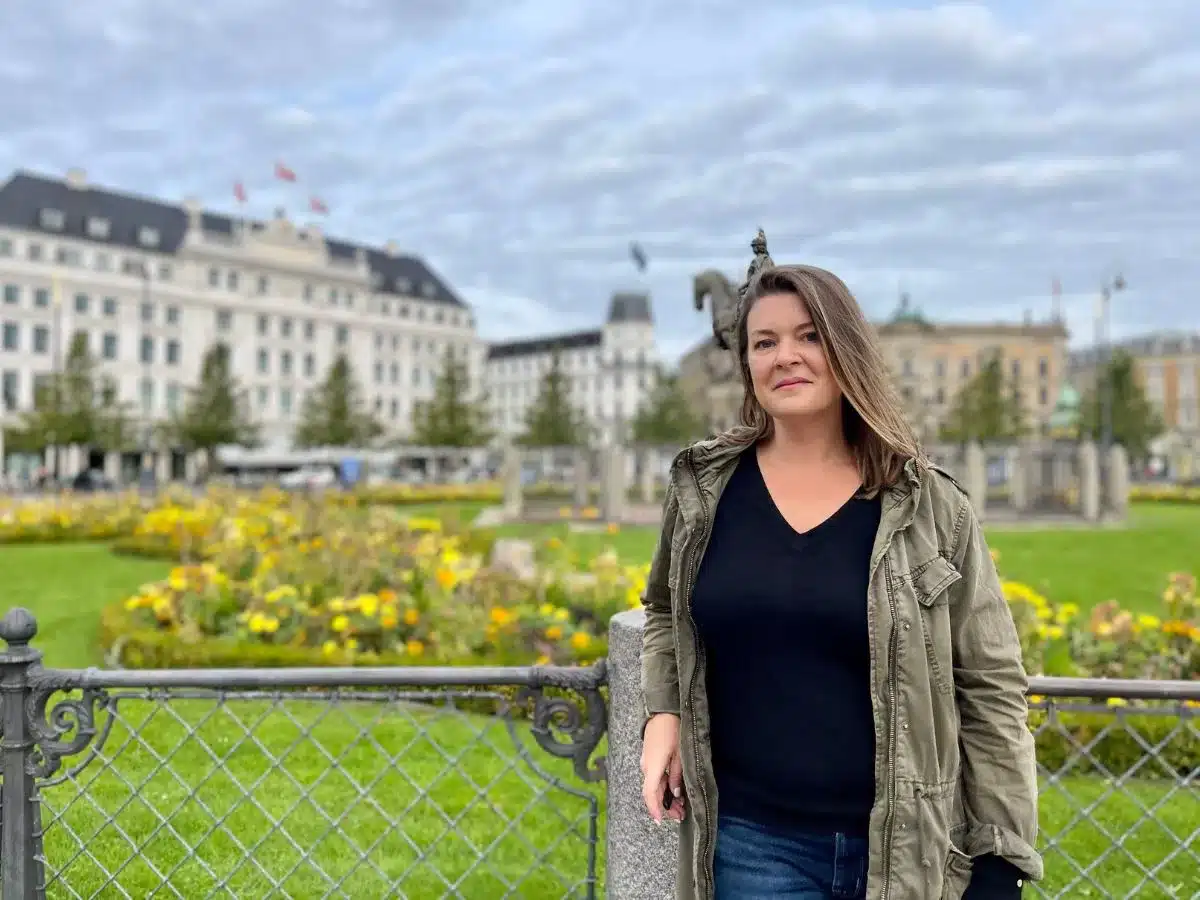 A woman standing alone in Copenhagen up against a fence. 