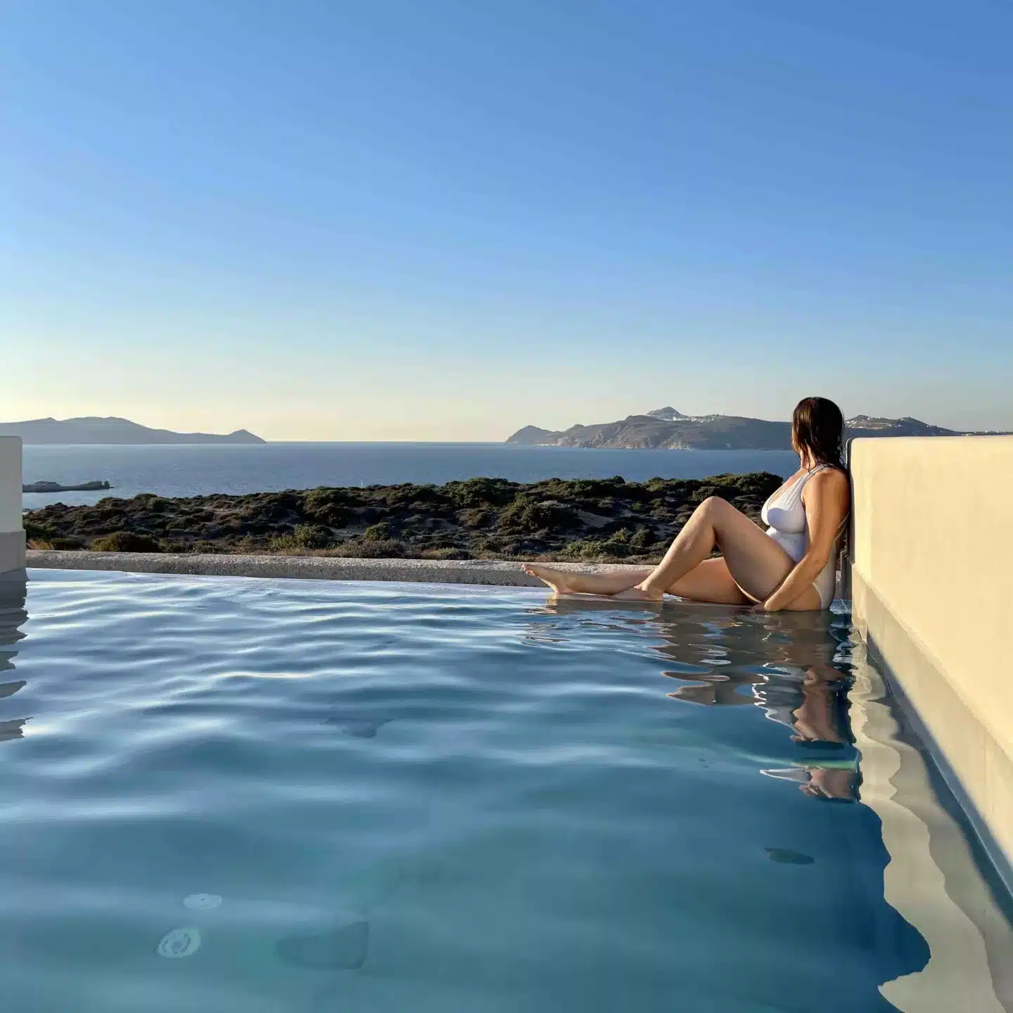 A woman sitting alone on a solo trip at the edge of a pool. 