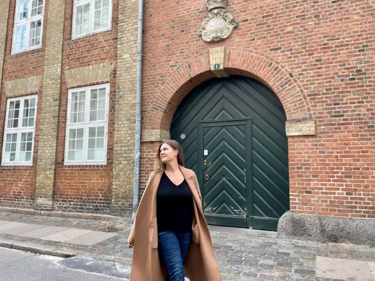 A woman alone in the street with brick wall and round doorway in the background. 